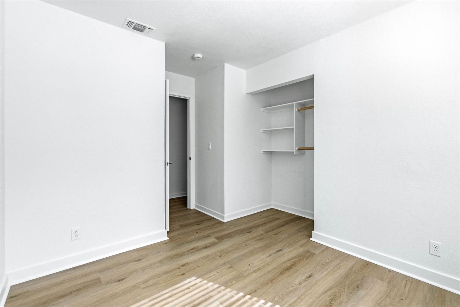 Empty bedroom with wood flooring and an open built-in closet.