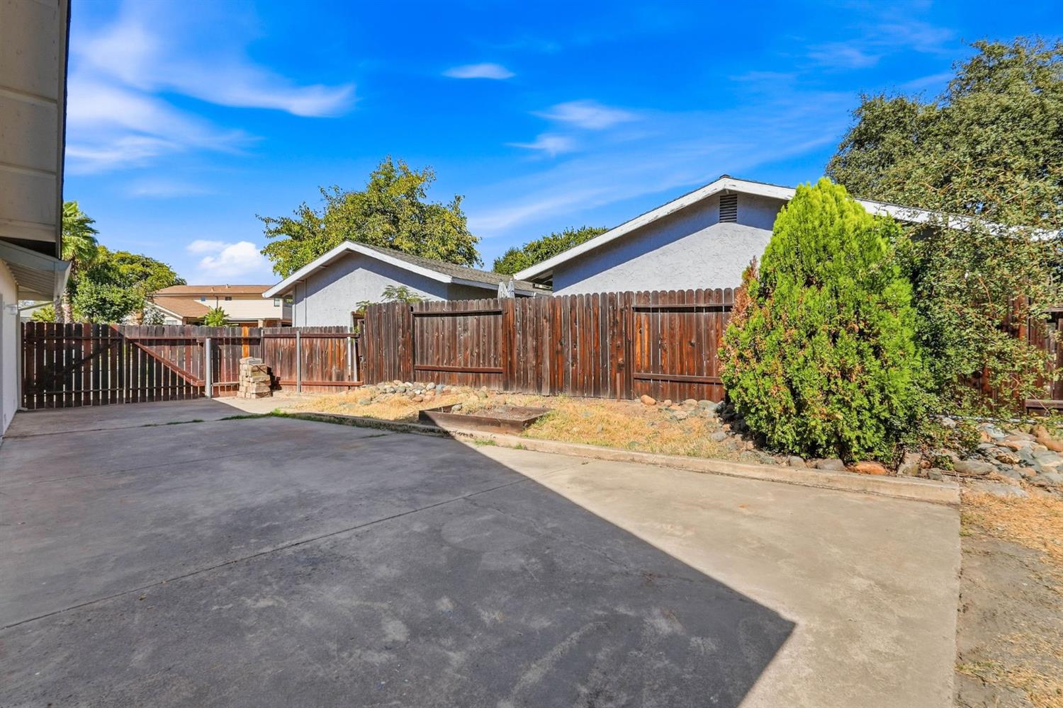 Paved patio enclosed by a wooden privacy fence, with a fire pit and dry landscaping.