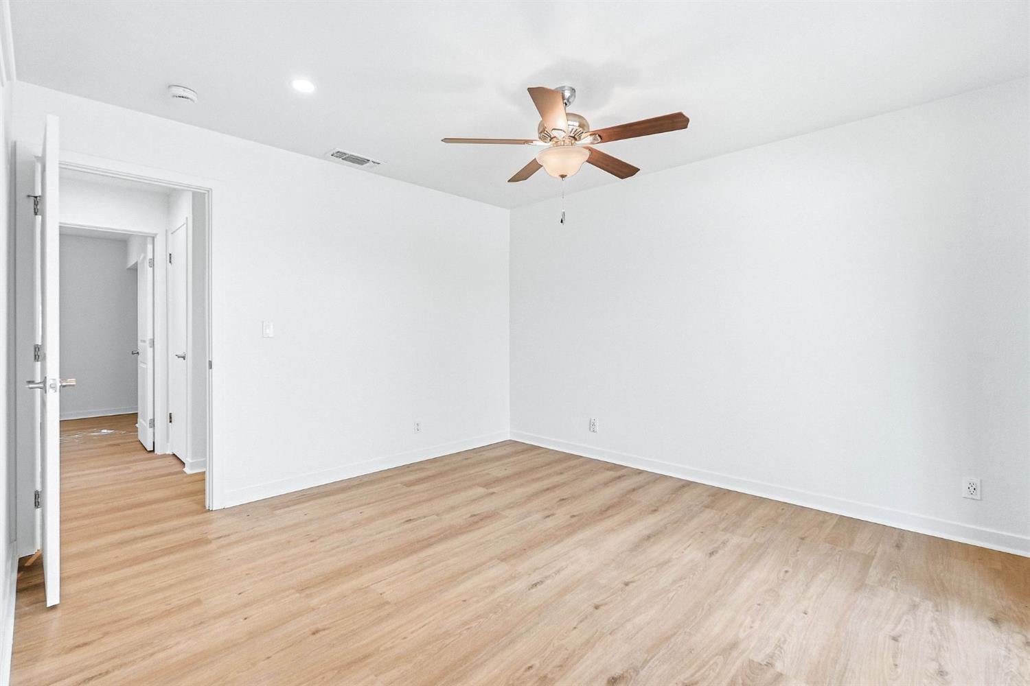 Empty room with light wood floors, white walls, and a ceiling fan with light.