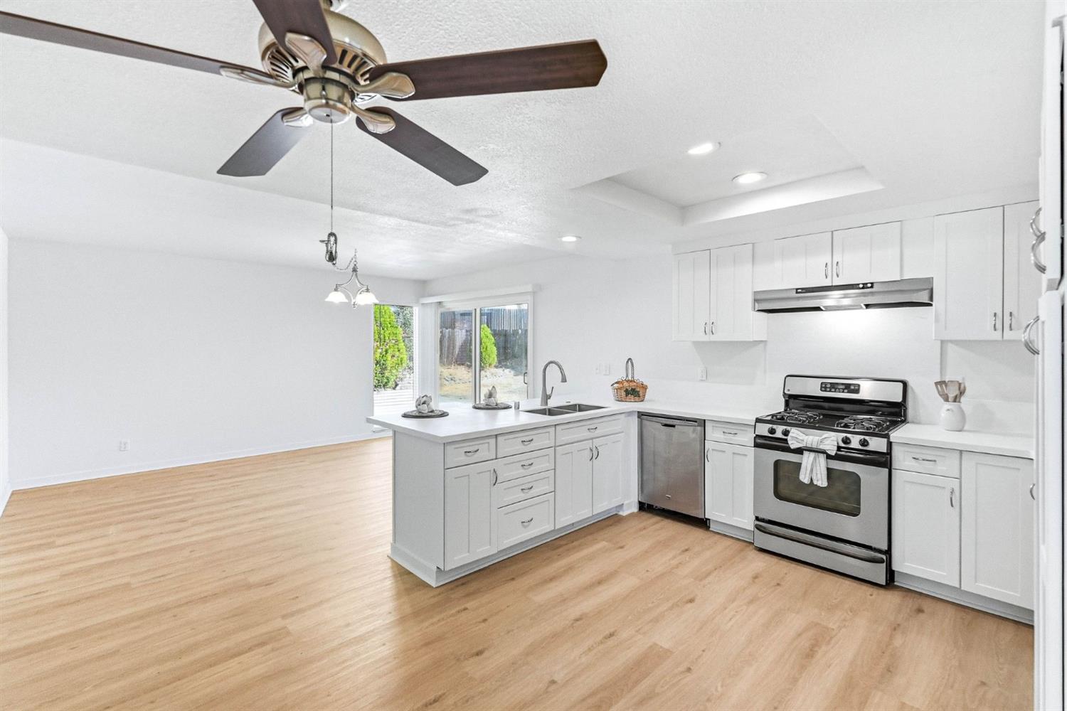 Open kitchen with white cabinets, stainless steel appliances, and a peninsula beside an unfurnished living area.