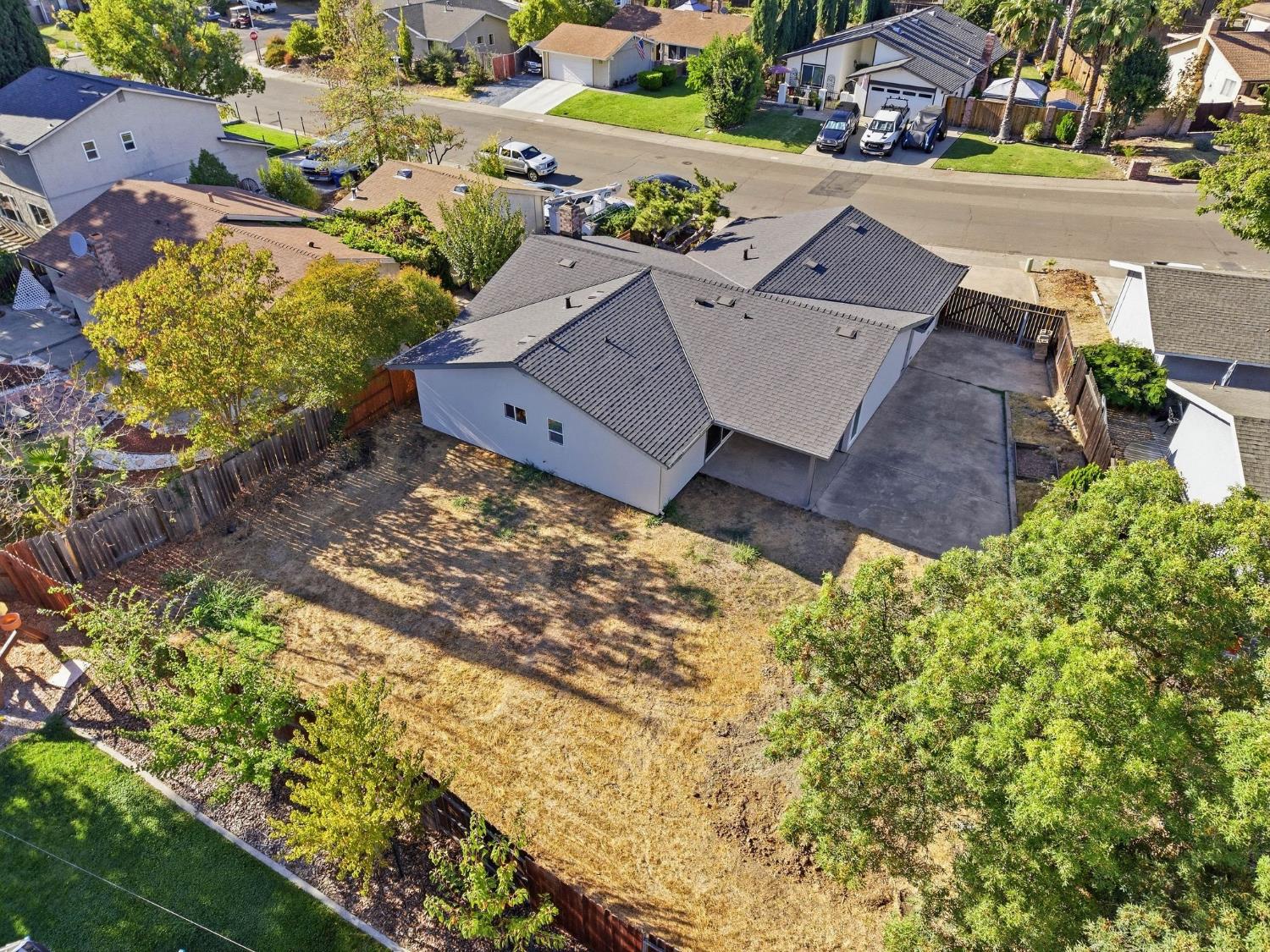Aerial view of a single-story home with a large fenced, mostly bare backyard and broad concrete driveway.