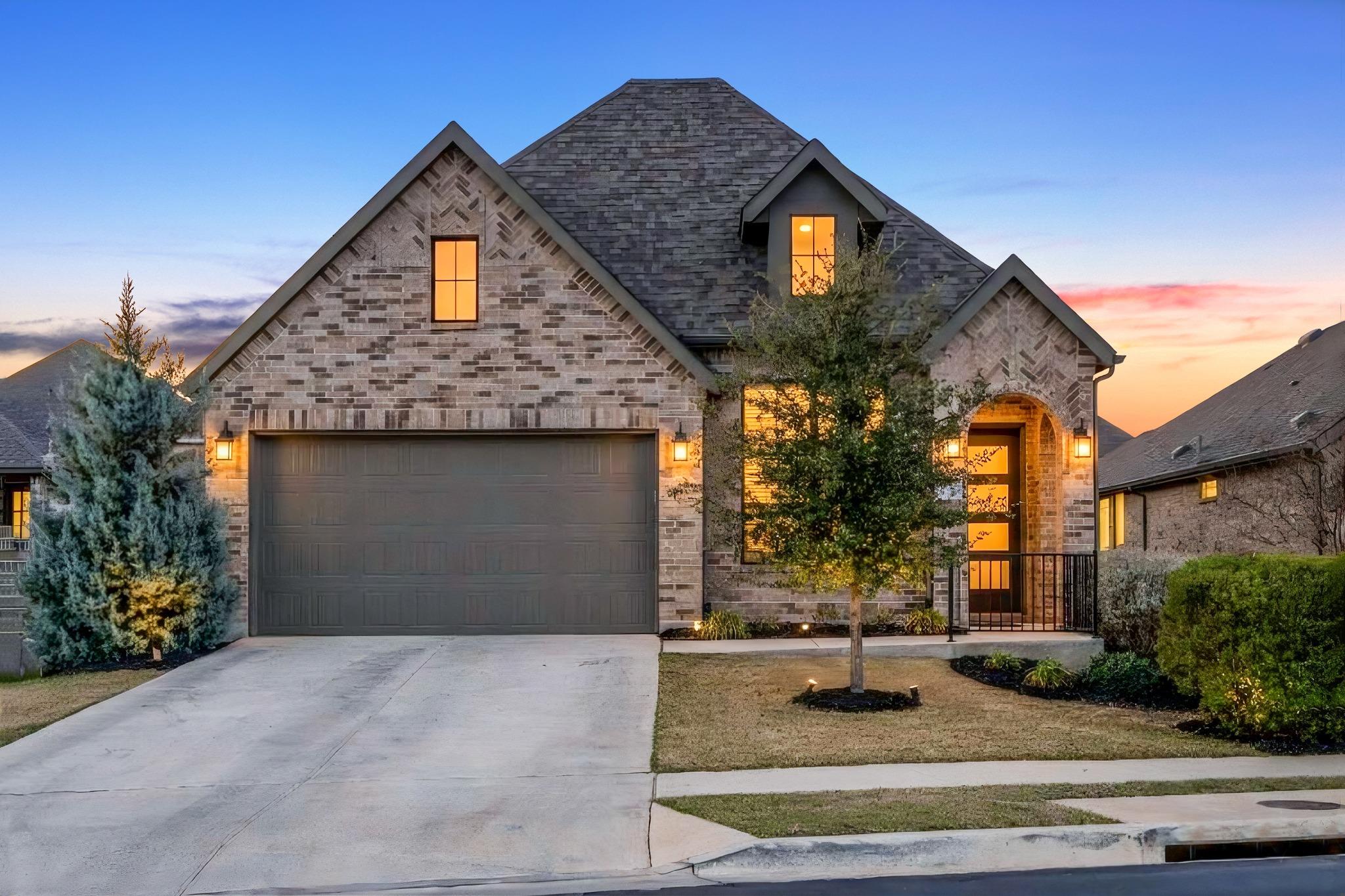 Two-story brick home with a broad driveway and warmly lit windows at dusk.
