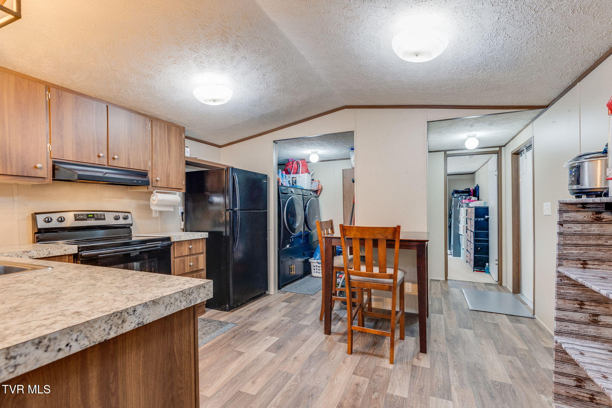 Kitchen with wood cabinets, black appliances, a dining table, and laundry area beyond