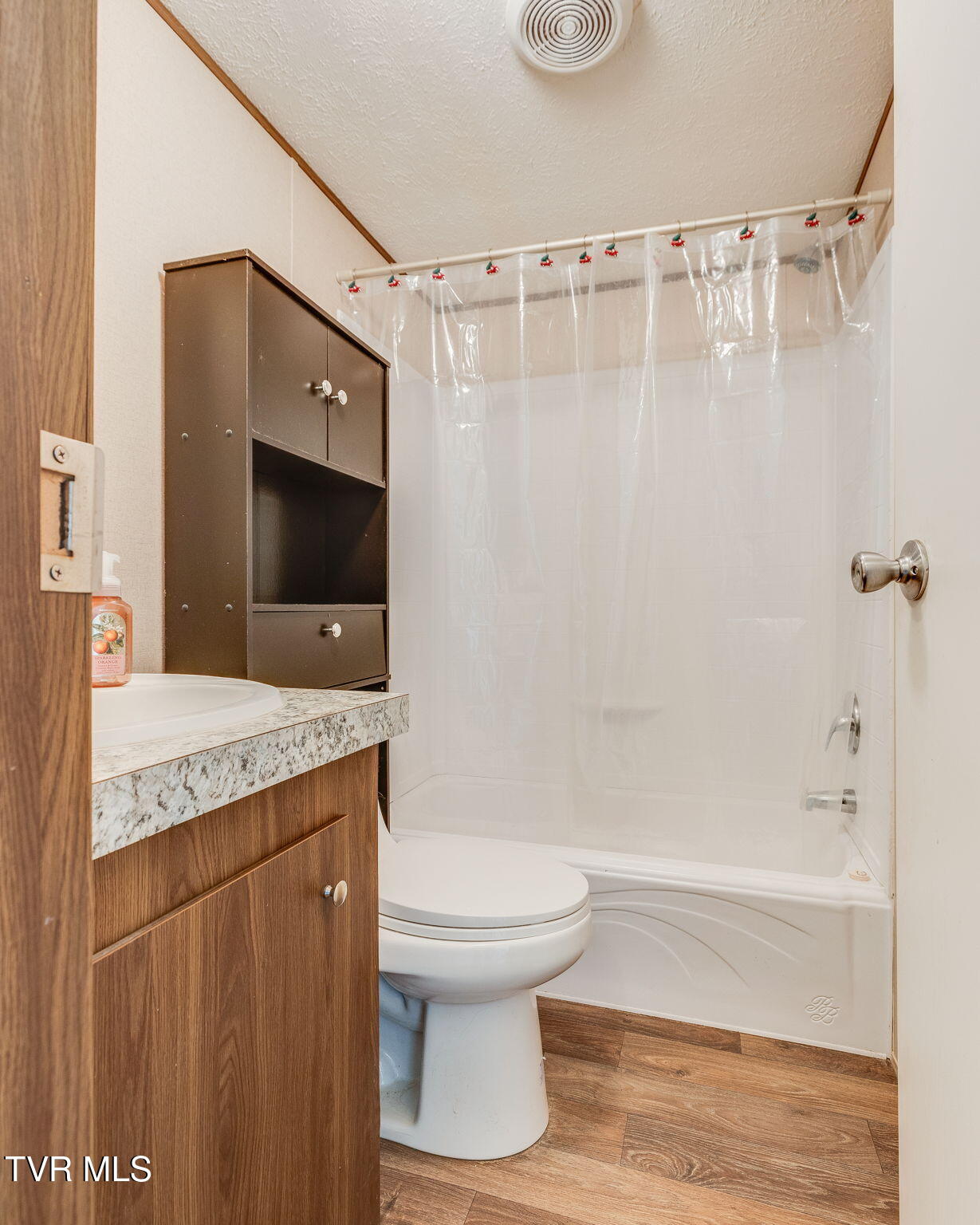 Bathroom with a wood vanity, toilet, and white tub-shower behind a clear curtain.