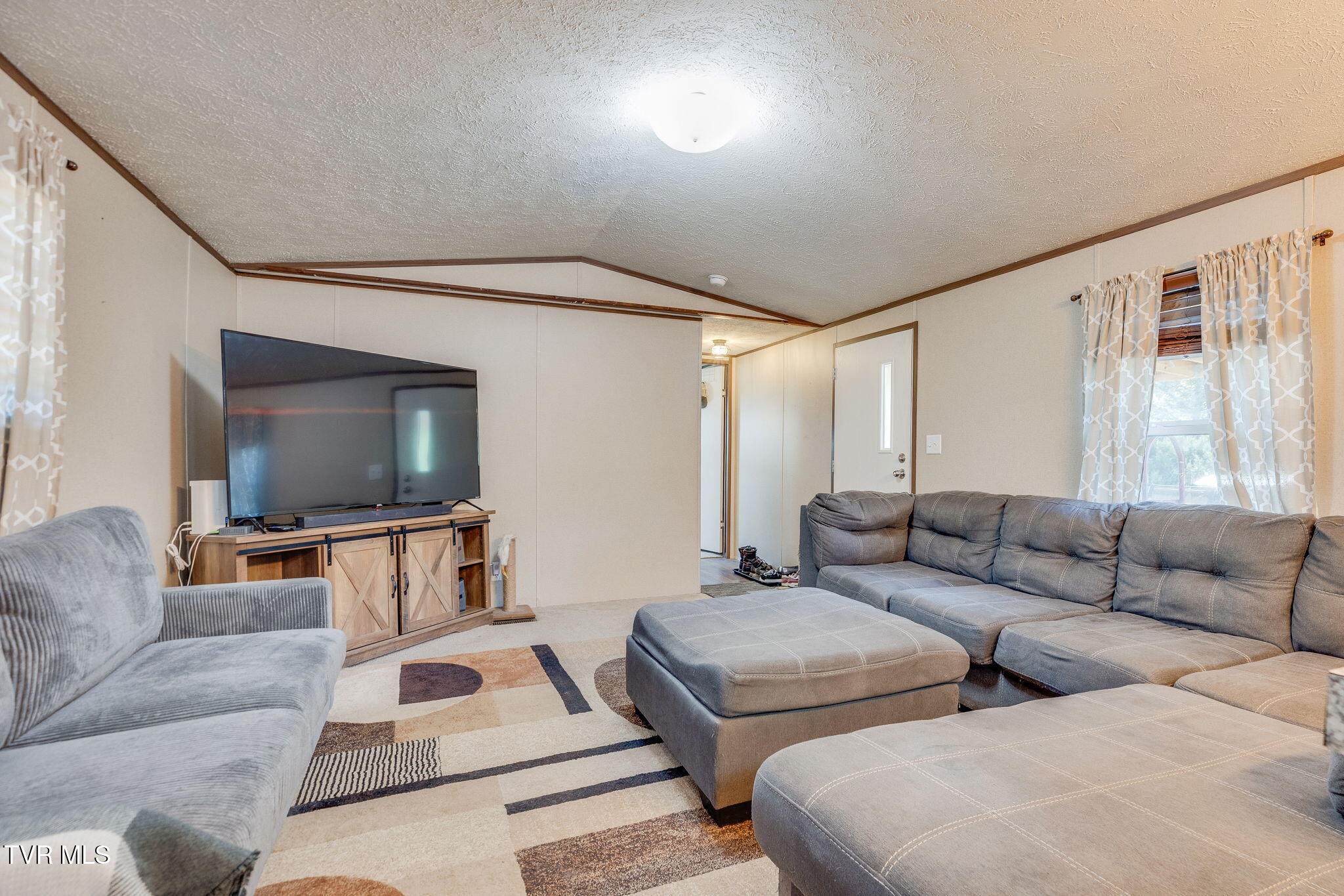 Living room with a gray sectional, matching ottoman, television, and geometric patterned rug.