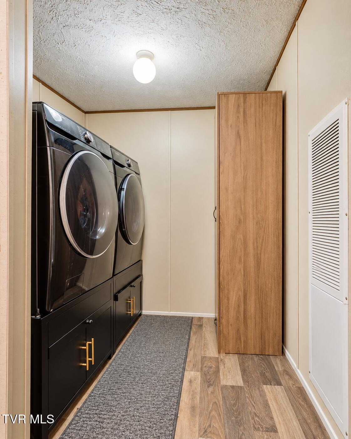 Laundry room with black front-loading washer and dryer, built-in cabinetry, and a tall wood-finish cabinet.