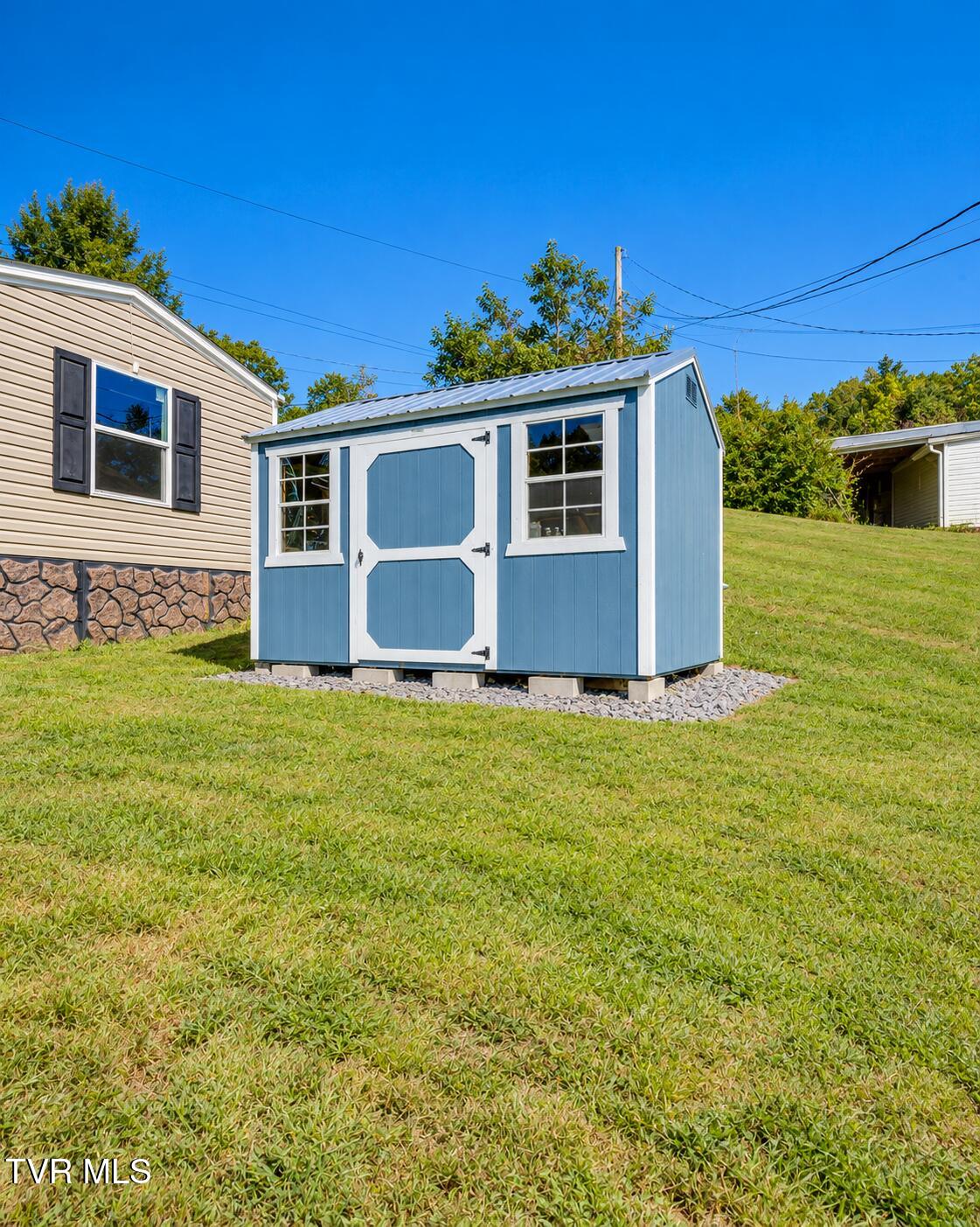 Blue storage shed with white trim and two windows on a grassy lawn.
