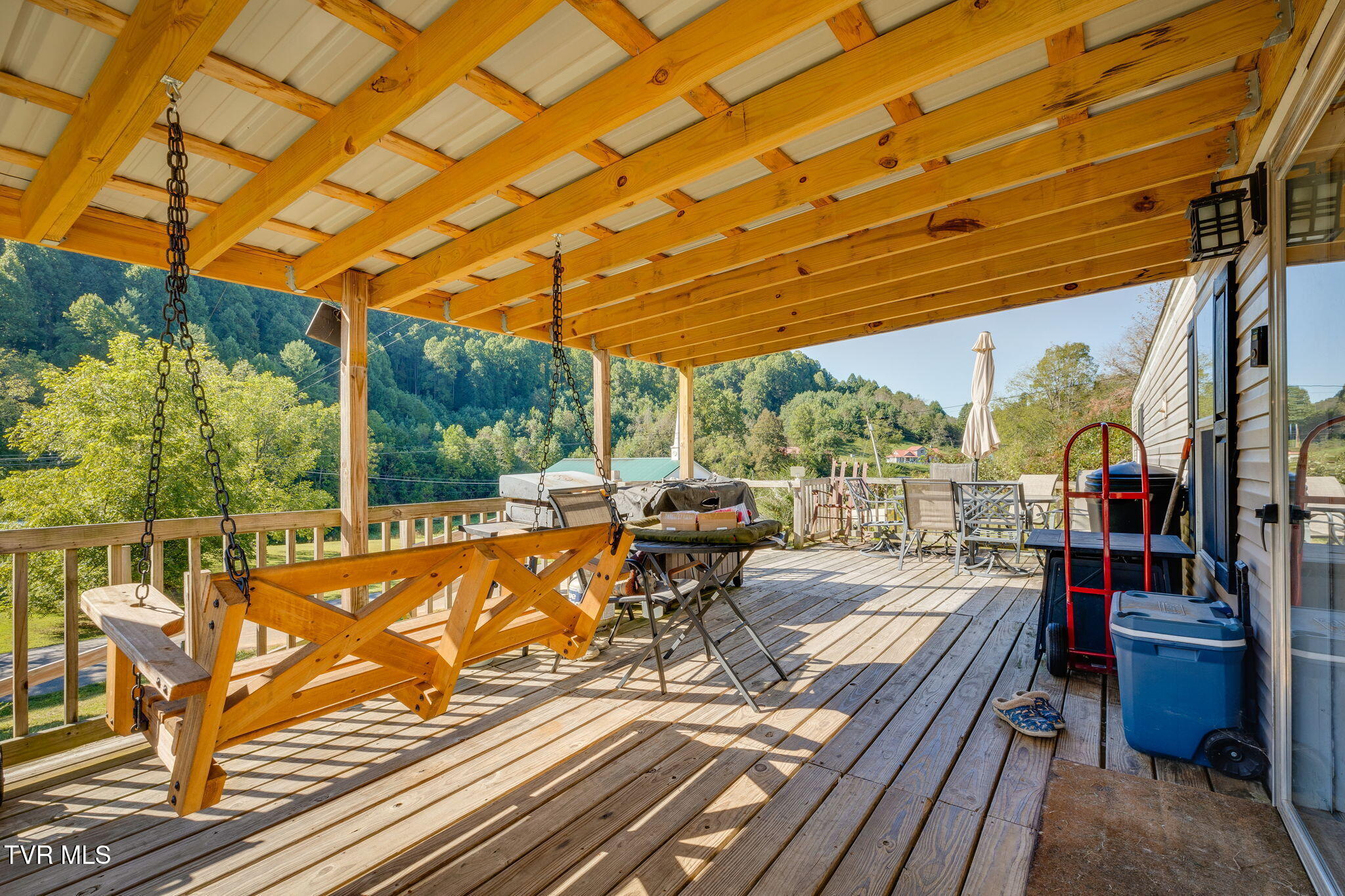 Covered wooden deck with a hanging swing and outdoor seating overlooking wooded hills.