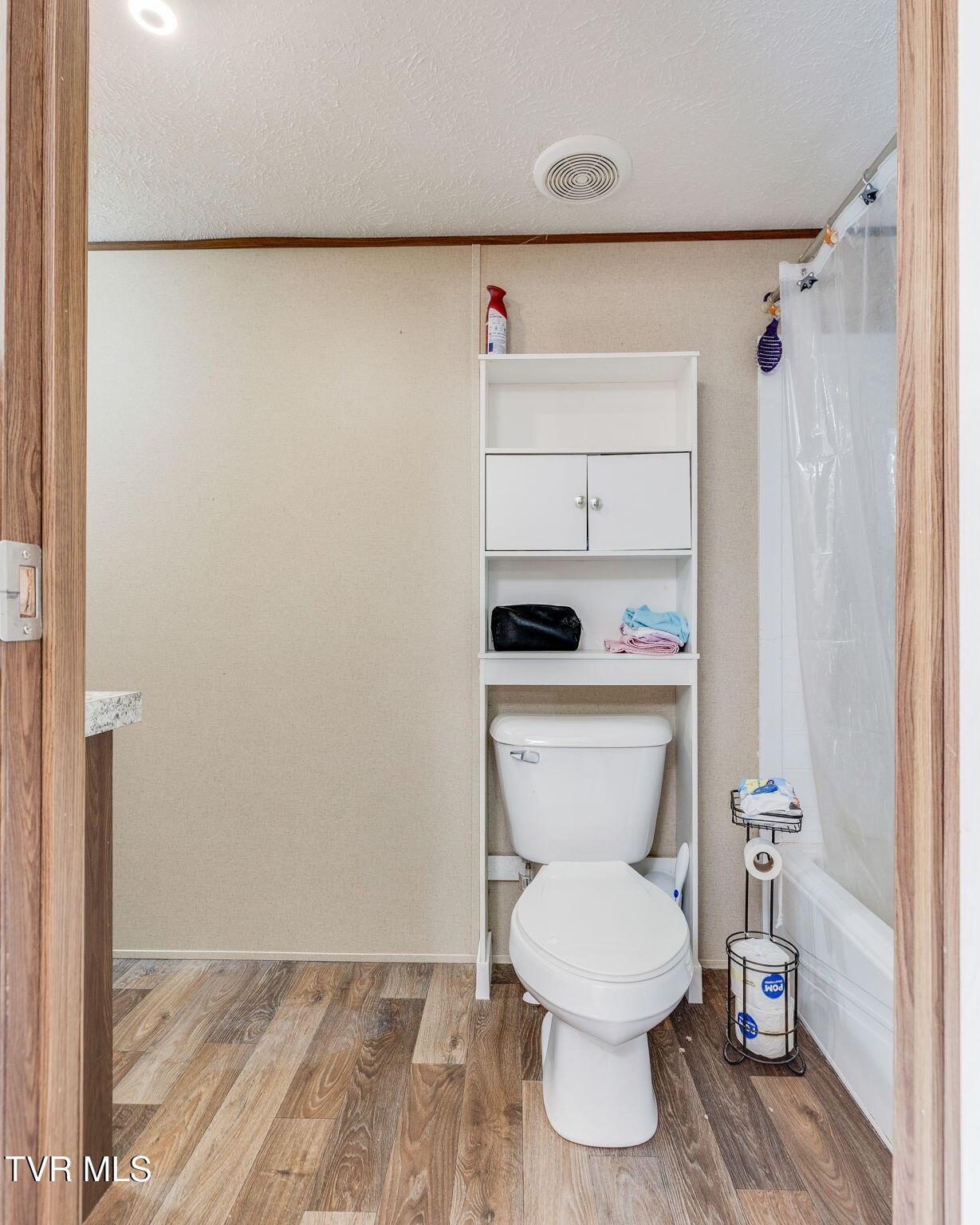 Bathroom with a toilet beneath built-in shelves and a bathtub with shower curtain.