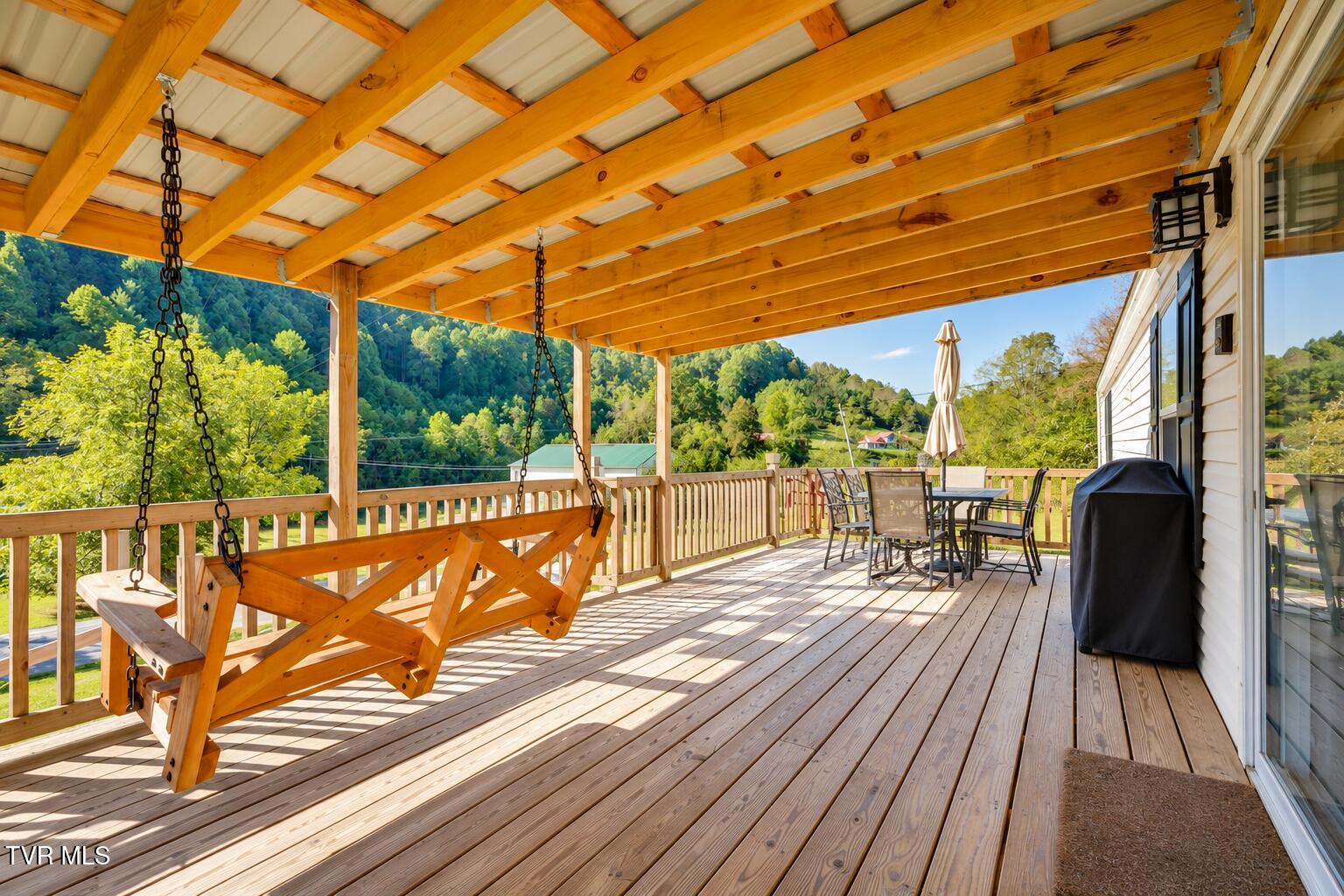 Covered wooden deck with a hanging swing and patio dining set overlooking wooded hills.