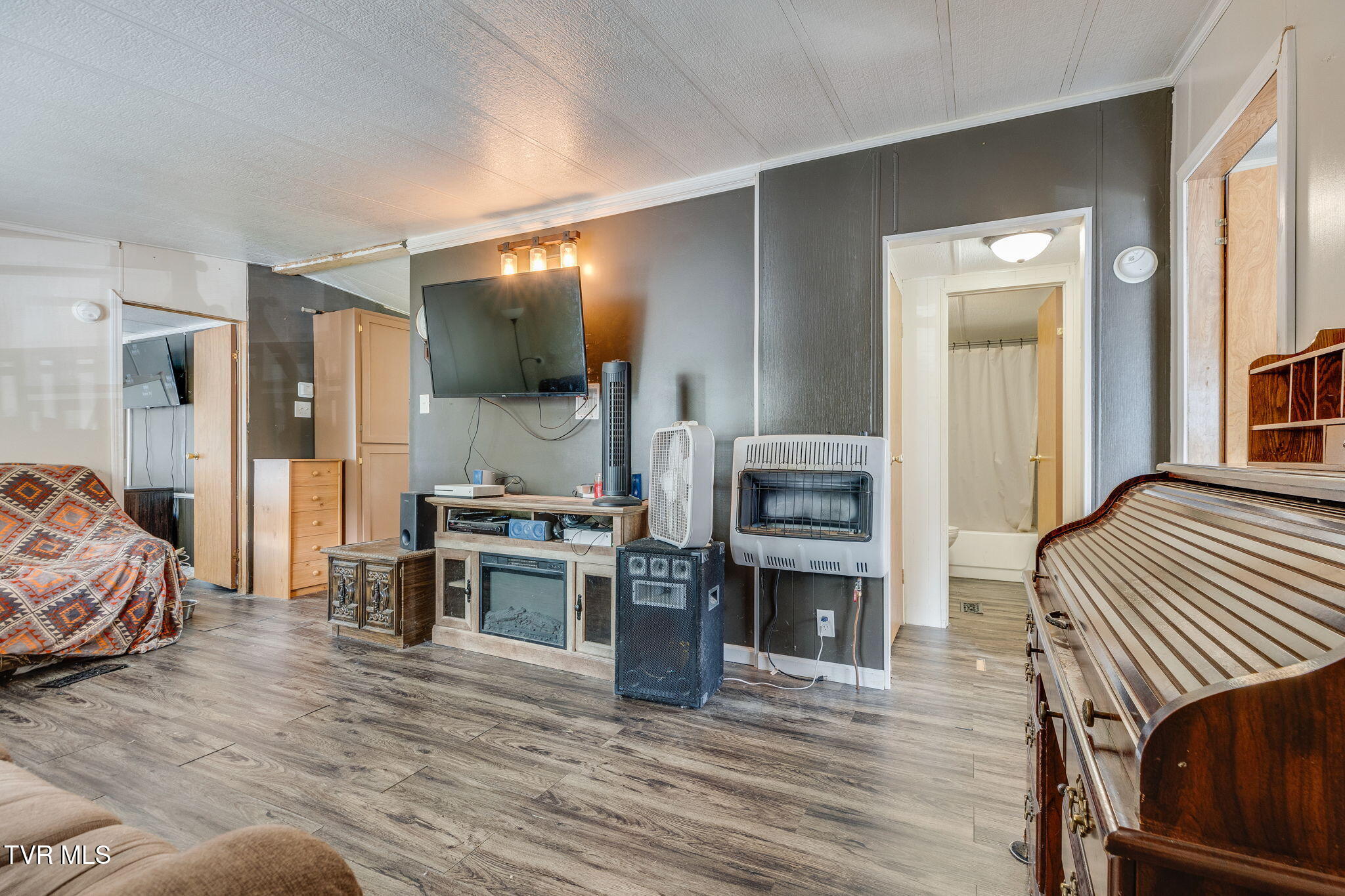 Furnished room with gray walls, wood-look flooring, wall-mounted television, portable heaters, and wooden bed frame.