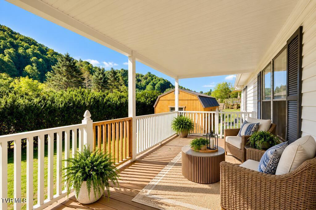Covered porch with wicker seating, potted ferns, and views of wooded hills.