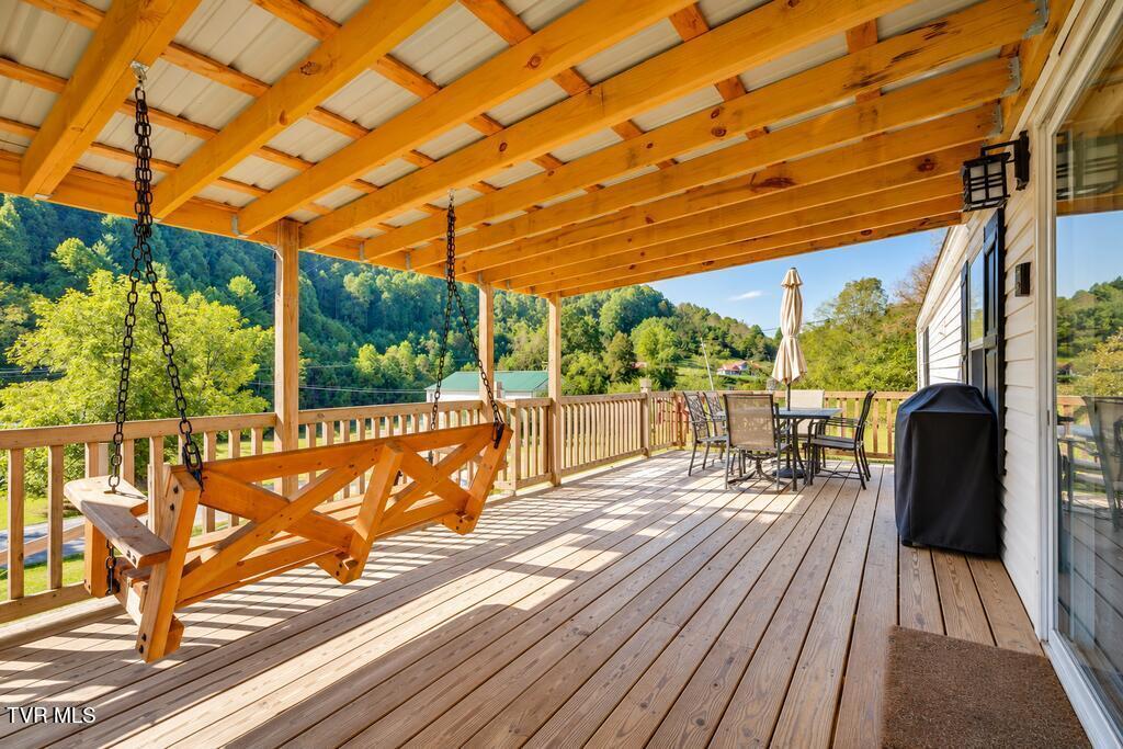 Covered wooden deck with a hanging swing and outdoor dining set overlooking wooded hills.