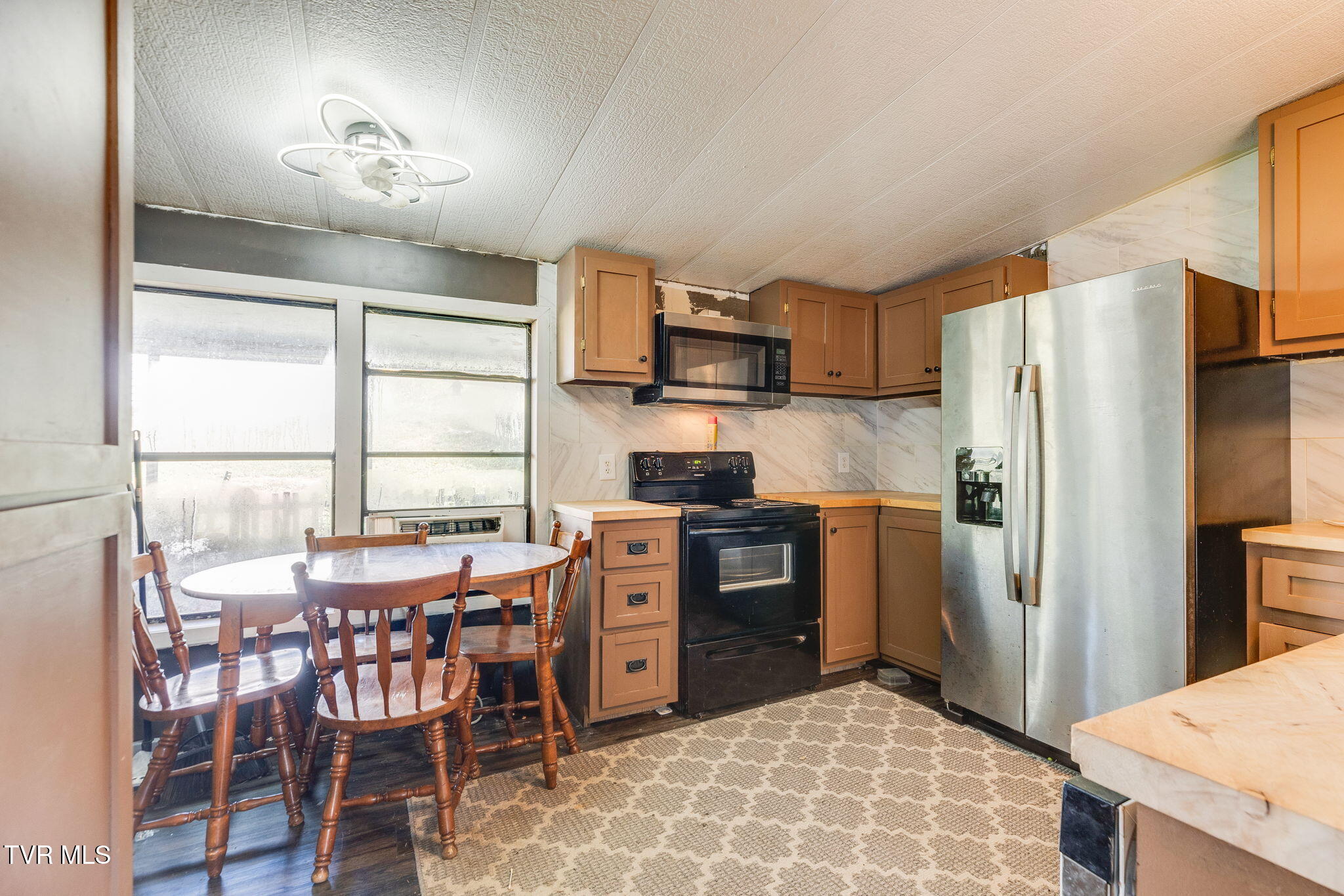 Kitchen with brown cabinets, stainless steel refrigerator, black appliances, and a round dining table by the windows.