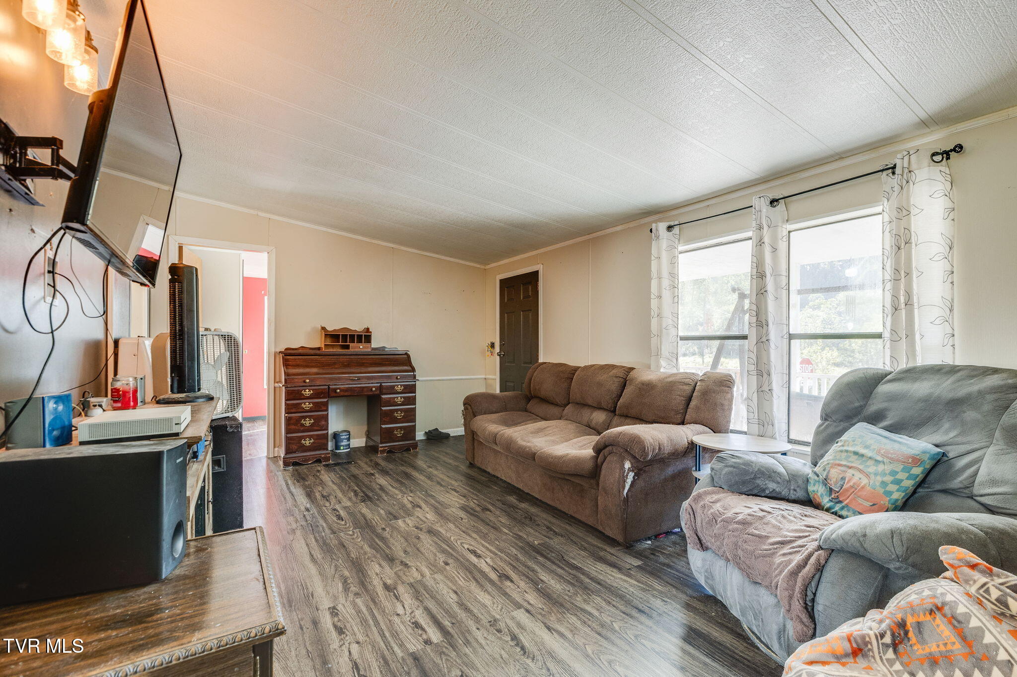 Living room with brown sofa, gray recliner, wooden desk, and bright curtained windows.