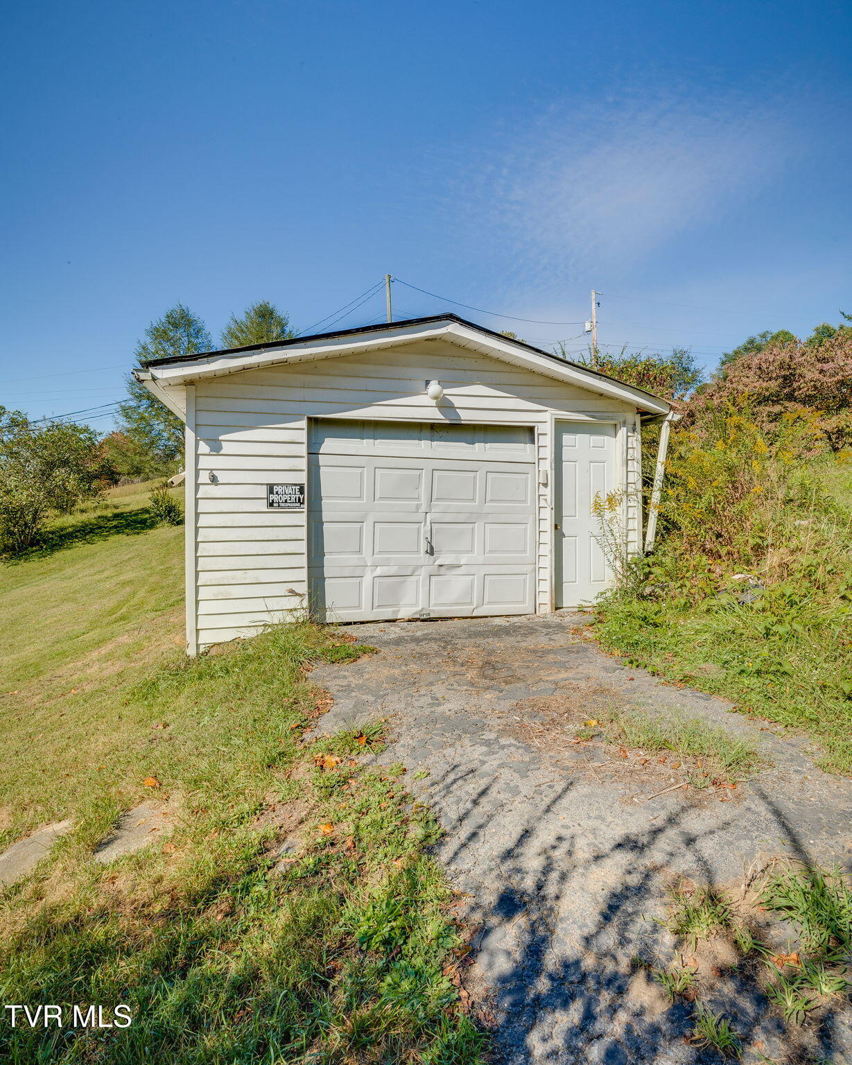 Detached white garage with a wide paneled door, side entrance, and cracked driveway.
