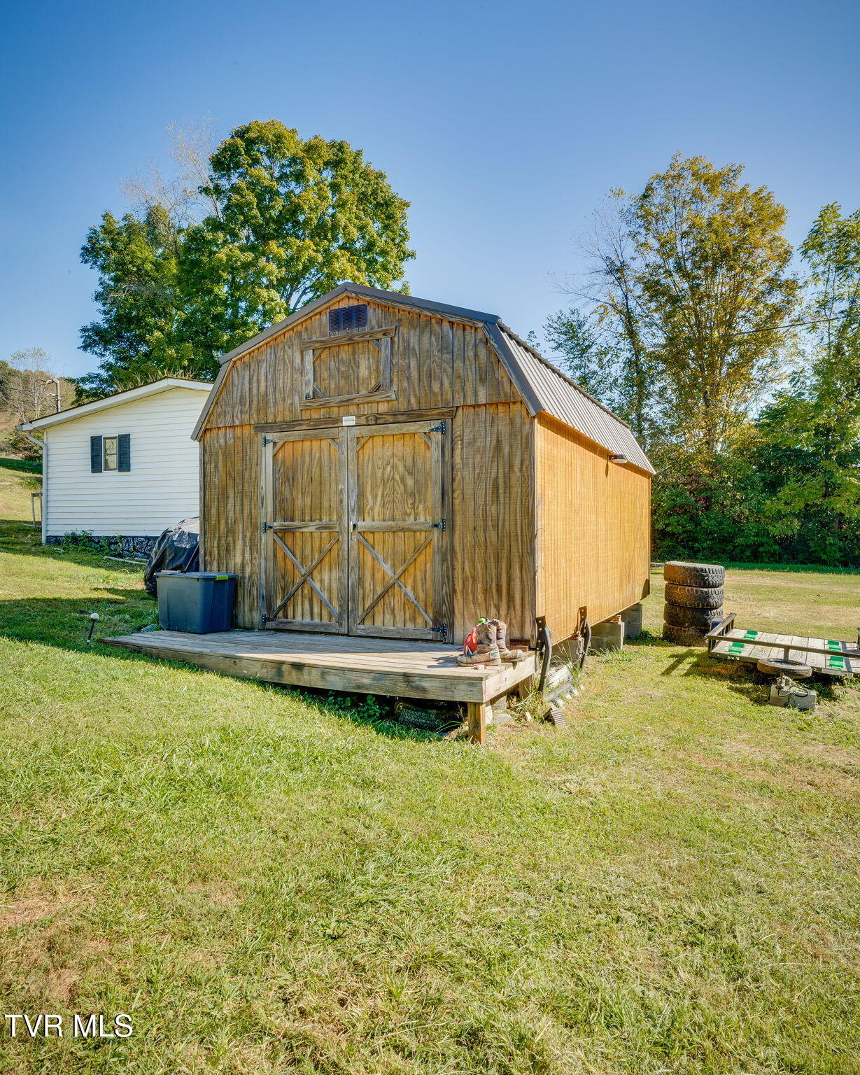 Wooden storage shed with double doors and a raised platform beside a white house.