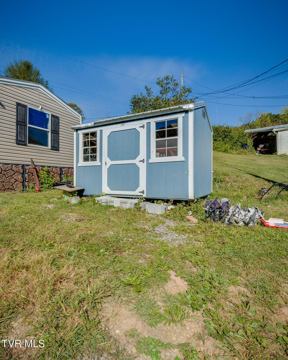 Blue storage shed with white trim and two windows in a grassy yard.