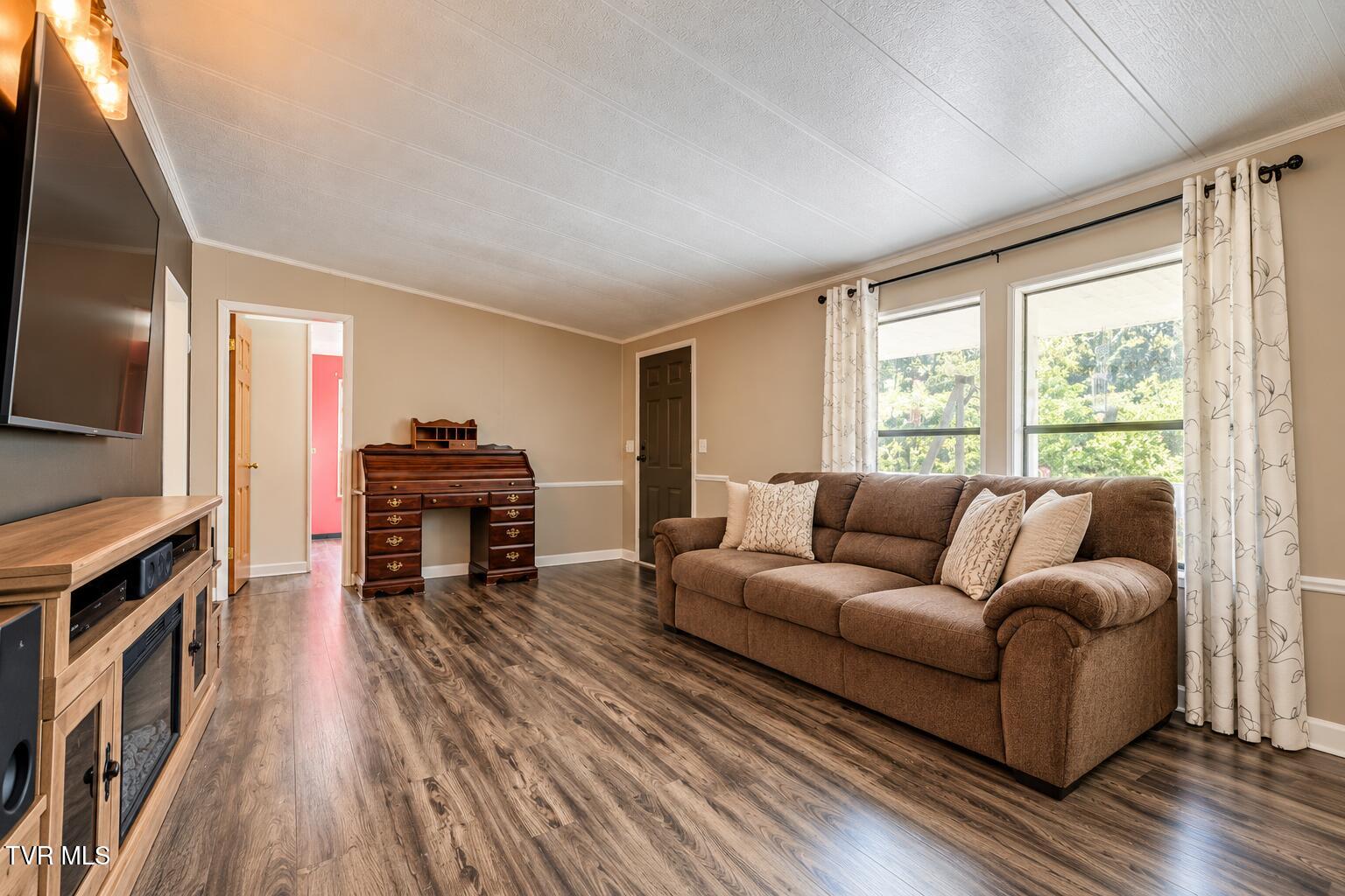 Living room with a brown sectional, dark wood writing desk, and large curtained windows.
