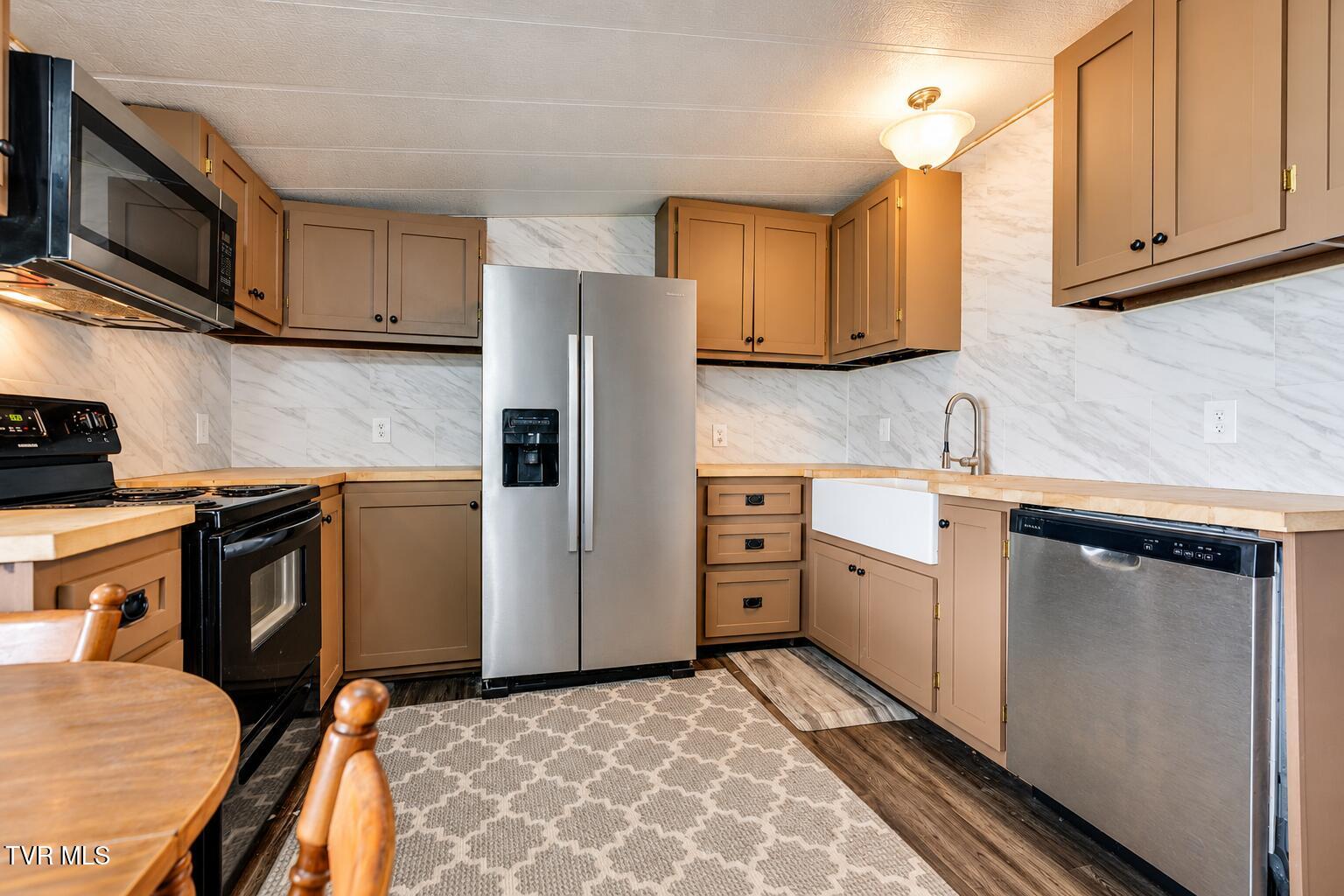 Kitchen with brown cabinets, marble-pattern backsplash, stainless appliances, and a farmhouse sink.