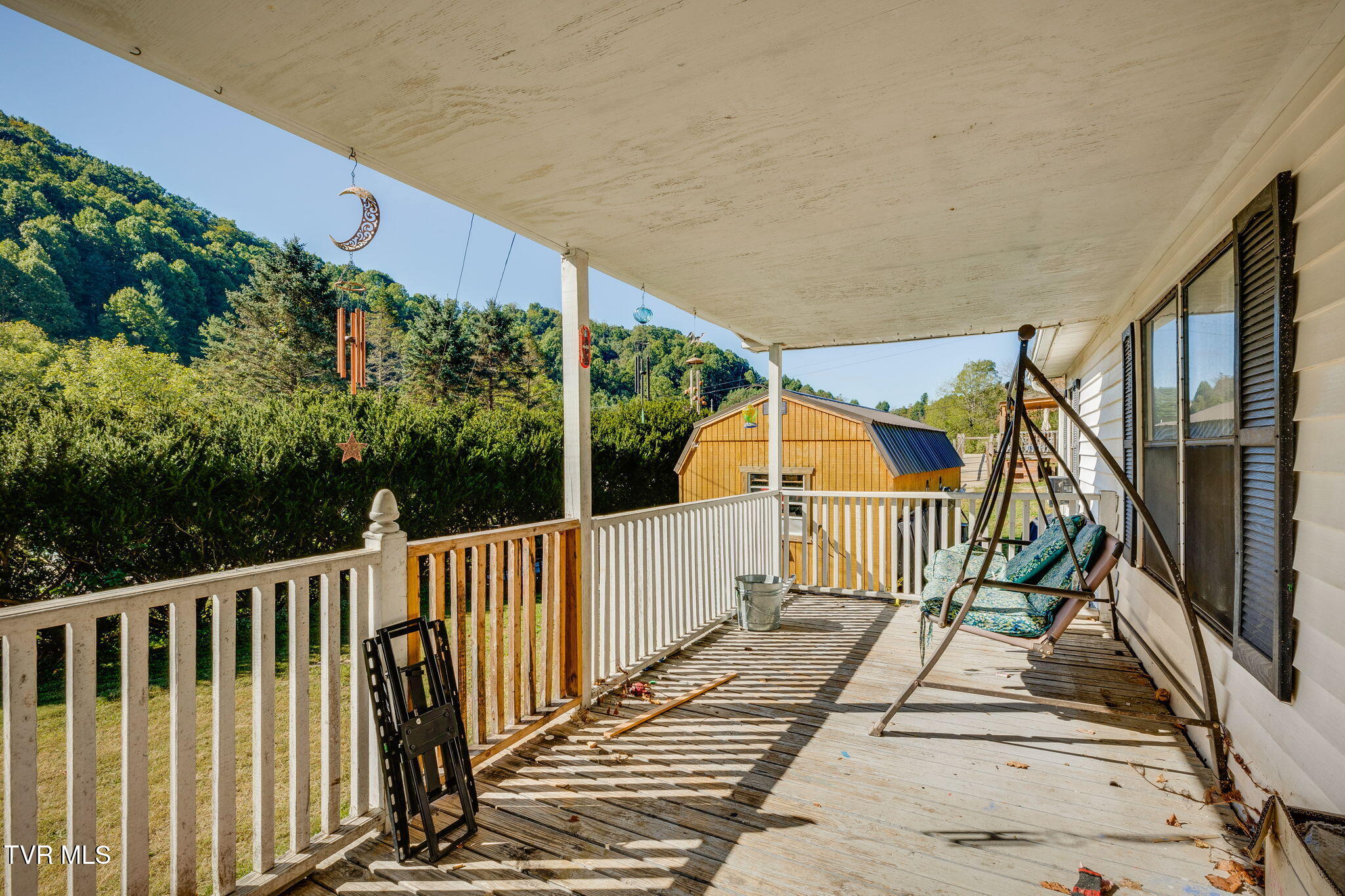 Covered wooden porch with a cushioned swing and wooded hillside views.