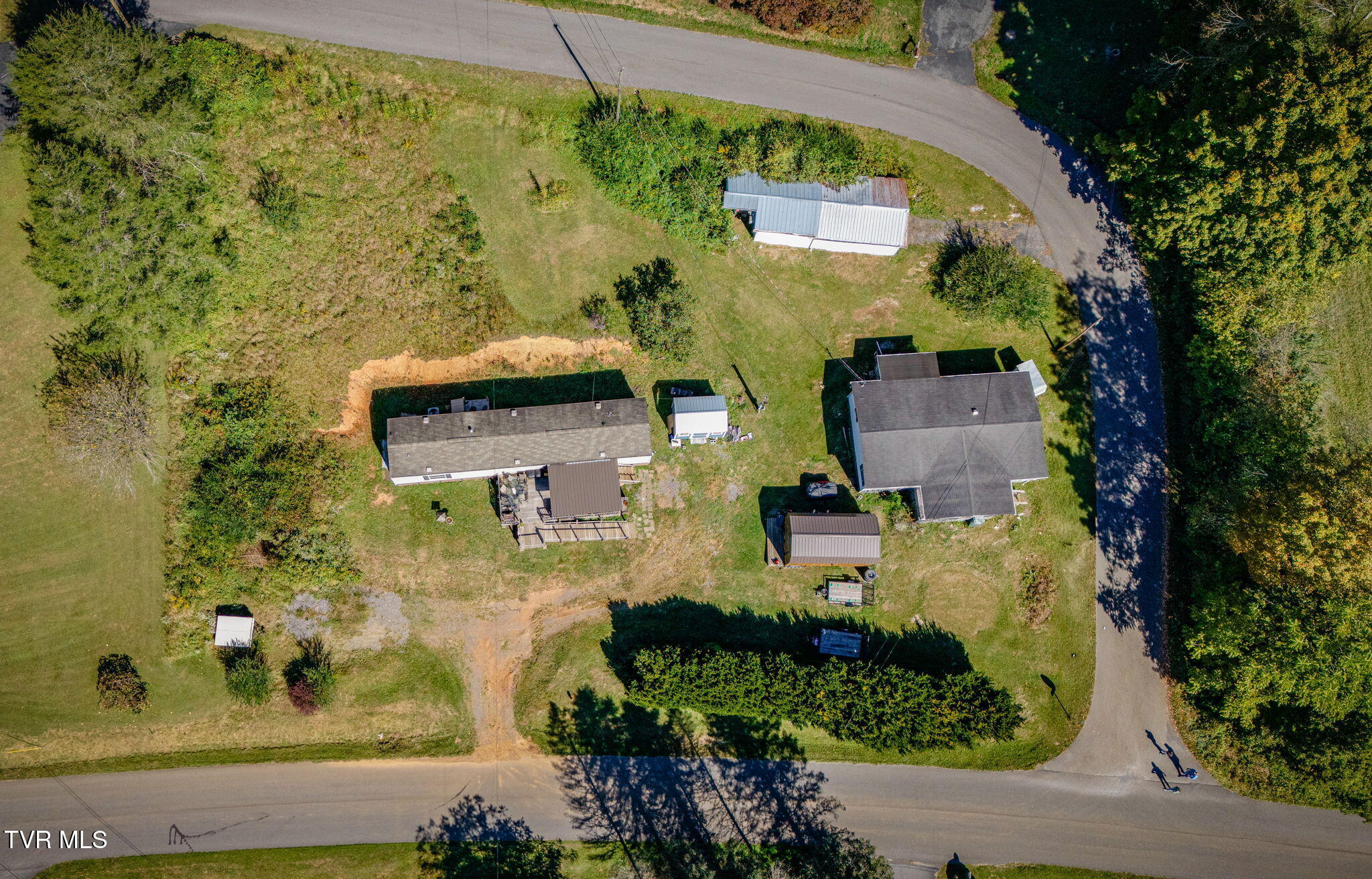 Aerial view of two homes and outbuildings on a grassy lot between two roads.