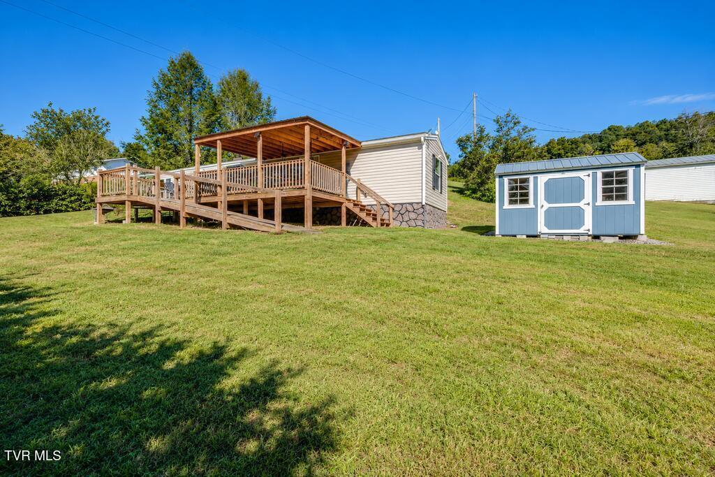 Small home with a covered wooden deck and blue storage shed on a grassy lot.
