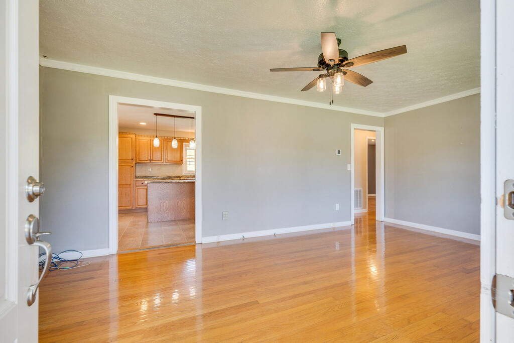 Unfurnished living room with polished hardwood floors, a ceiling fan, and a doorway to the kitchen.