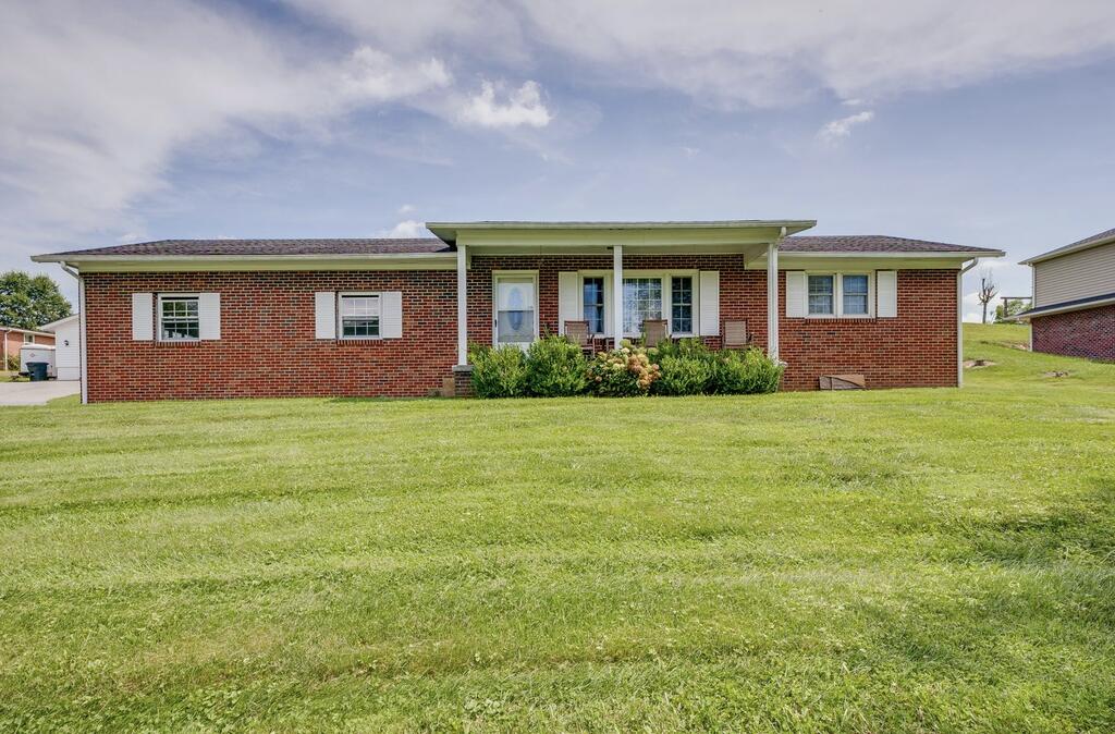 Red brick ranch home with a covered porch and broad green lawn.