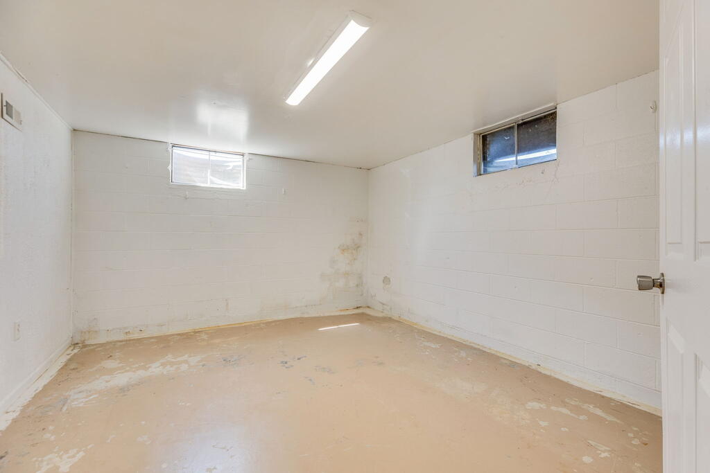 Empty unfinished basement room with white block walls, a worn floor, and two small high windows.