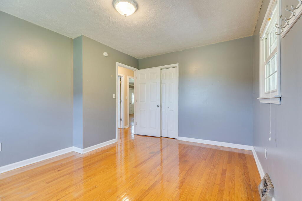 Vacant bedroom with gray walls, hardwood floors, and white closet doors.