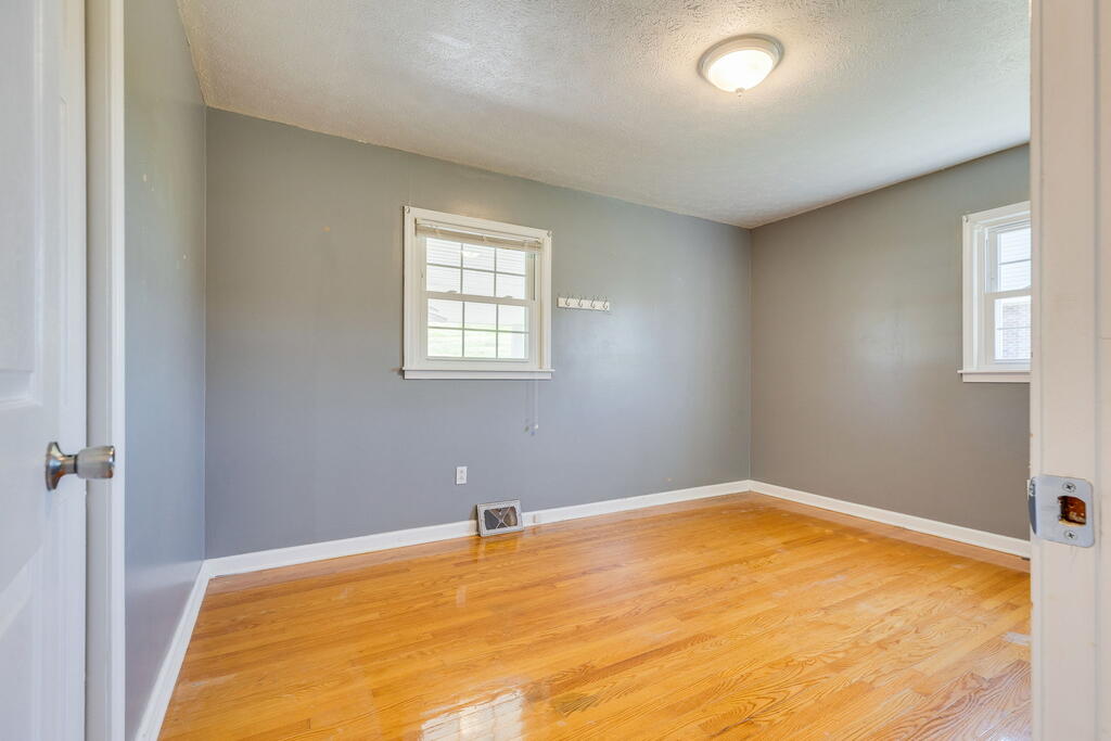 Empty room with gray walls, two windows, and polished hardwood floors.