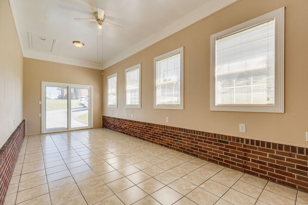 Empty tiled room with brick wainscoting, multiple windows, and a sliding glass door.