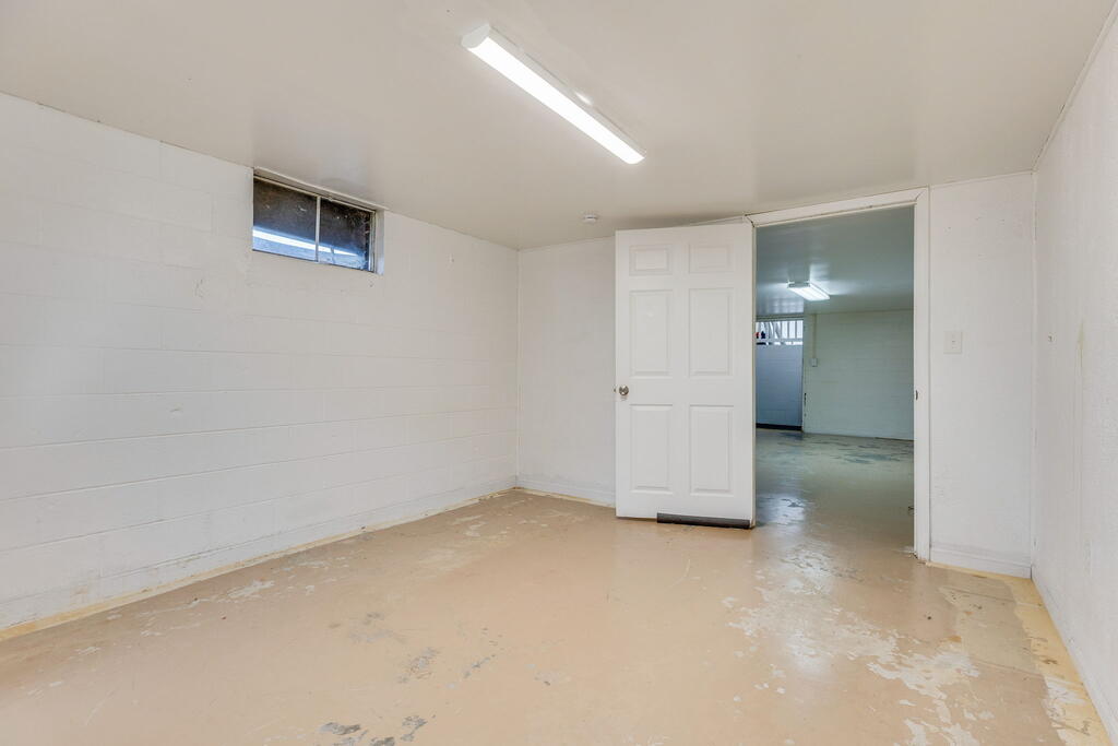 Empty unfinished room with white walls, a worn floor, and an open doorway to another room.