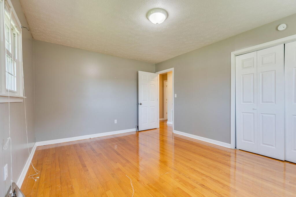 Empty room with polished hardwood floors, gray walls, a window, and double closet doors.