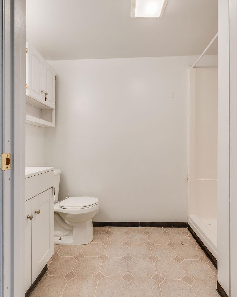 Bathroom with a white vanity and toilet, bathtub, and beige hexagonal floor tiles.
