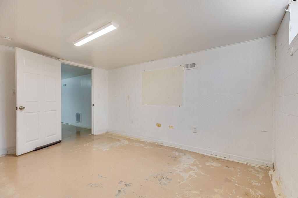 Vacant room with an open doorway, fluorescent light, and a worn, peeling floor.