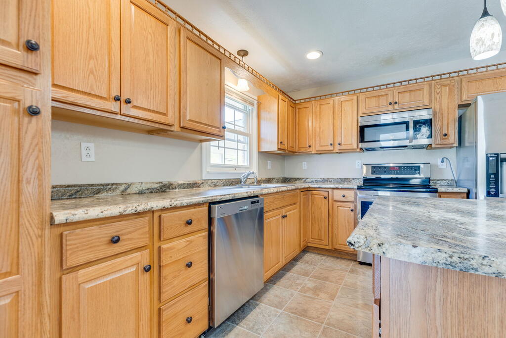 Kitchen with honey-colored wood cabinets, granite counters, a central island, and stainless steel appliances.
