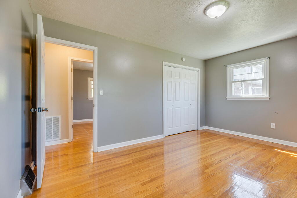 Empty bedroom with hardwood floors, a double-door closet, and a window.