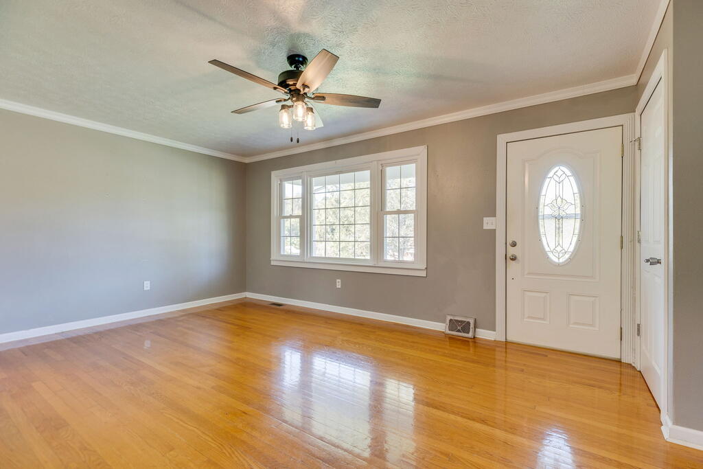 Vacant room with polished hardwood floors, a ceiling fan, large window, and front door with oval glass.