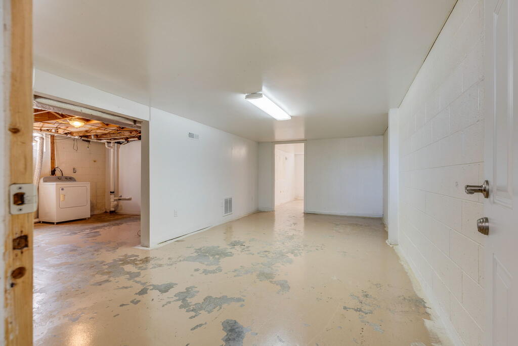 Vacant basement room with a worn concrete floor and an adjoining laundry area with a dryer.