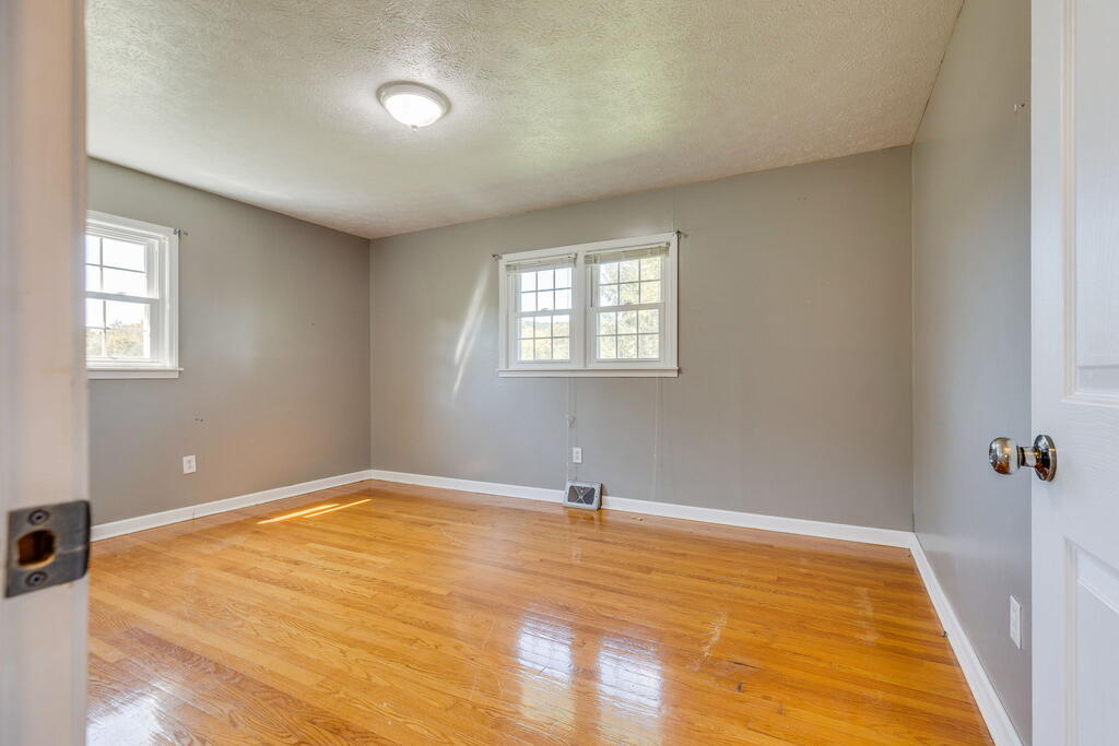 Empty room with glossy hardwood floors, gray walls, and two windows.