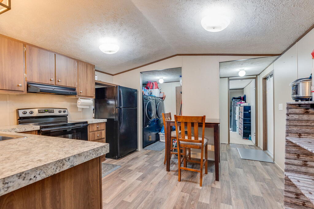 Kitchen and dining area with wood cabinets, stone-pattern counters, and a washer and dryer visible through the doorway.
