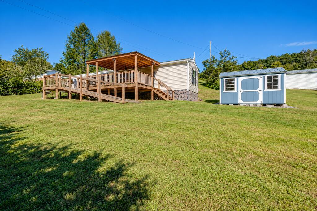 Home with a covered wooden deck and a blue storage shed on a broad lawn.