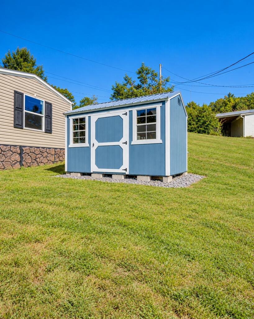 Blue storage shed with white trim and double doors beside a beige home.