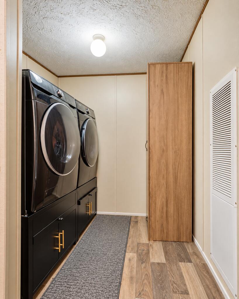 Laundry room with black front-loading washer and dryer, built-in cabinets, and wood-look flooring.