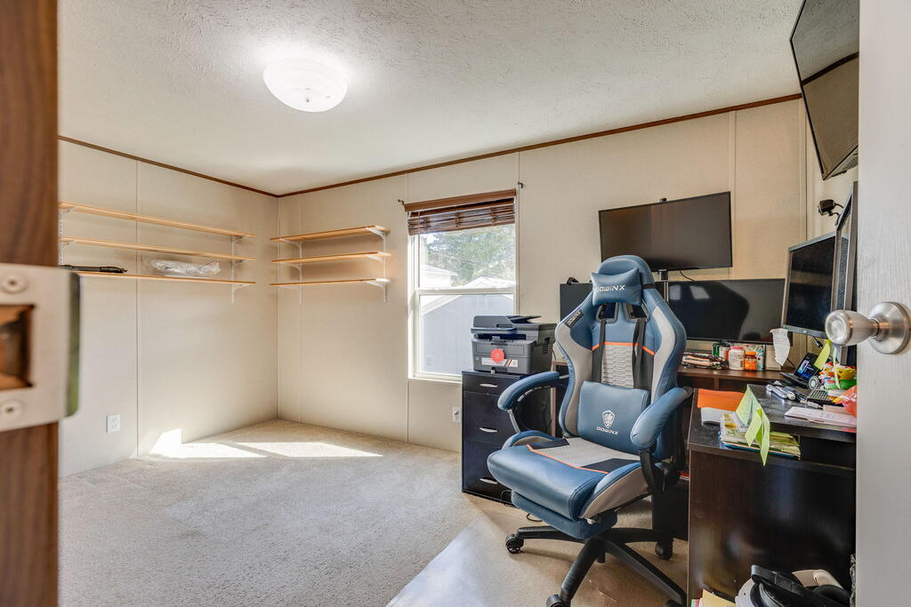 Home office with open wall shelves, a window, and a desk with multiple monitors.