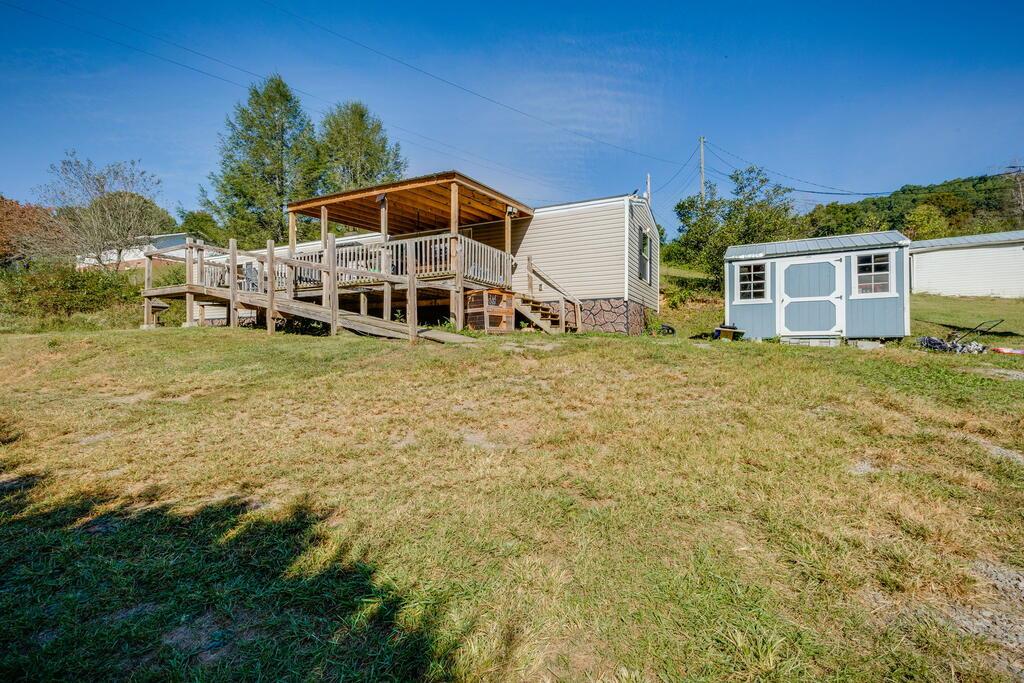 Mobile home with a covered wooden deck and small blue shed in a grassy yard.