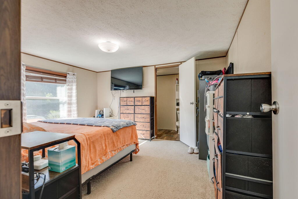 Bedroom with an orange quilted bed, window, dressers, and wall-mounted television.