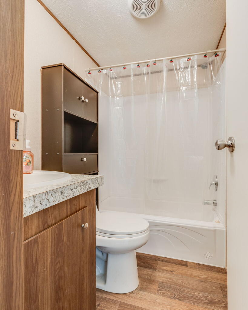 Bathroom with a wood vanity, dark wall cabinet, toilet, and tub-shower with clear curtain.